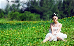 Asiatisches Mädchen, das im Gras sitzt
